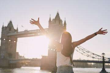 Woman, freedom and travel by the London bridge or city for holiday break or outdoor summer vacation. Joyful female tourist with open arms enjoying sunny adventure trip, traveling and sightseeing - Powered by Adobe
