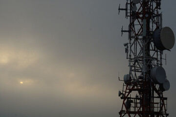 Television and mobile phone antenna at sunset with the sun in the fog