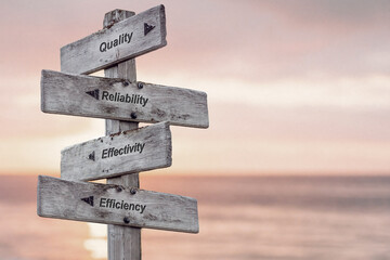 quality reliability effectivity efficiency text written on wooden signpost outdoors at the beach during sunset