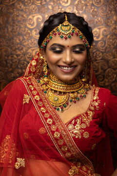 Shy Indian bridal woman Wearing Beautiful makeup dressed in Hindu traditional wedding Red lehenga. jewelry set which consisting necklace and head adornment (maang tikka)