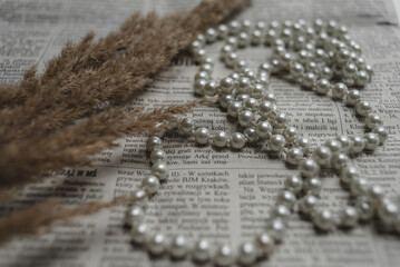 A string of pearls and gems lie on a newspaper, a photo in an elegant retro style.