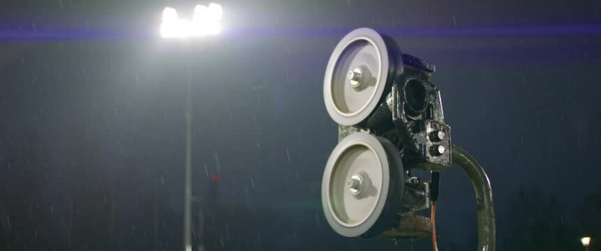 CU View Of Hand-fed Pitching Machine Standing On A Baseball Field Under Heavy Rain At Night