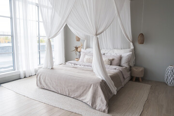 Bright Scandi-style interior in the bedroom. A canopy, a linen bed and a jute rug. Full-height windows