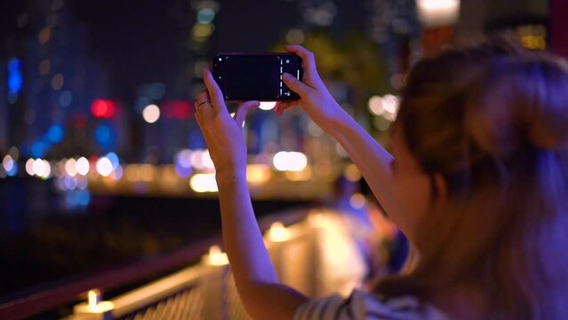Girl takes pictures of the skyscrapers of Dubai Marina on her phone