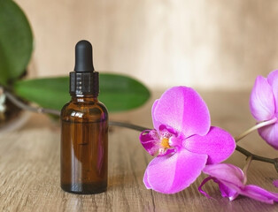 Fototapeta na wymiar Dark serum bottle with pipette on wooden textured table with a blooming purple orchid