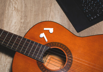 Classical guitar with laptop and headphones on a wooden textured table, close-up. Online learning concept