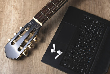 Guitar part with laptop and headphones on wood textured table, close-up. Online instruction