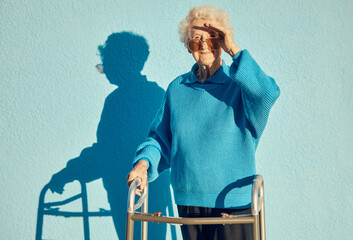 Portrait, shadow and disability with a senior woman on a blue wall background while holding a mobility walker outdoor. Health, handicap and fashion with a mature female standing outside alone - obrazy, fototapety, plakaty