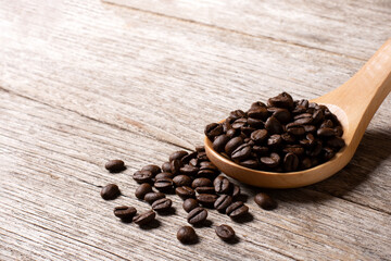 Coffee beans in wooden spoon isolated on rustic wooden table background.
