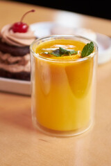 Matcha with orange in a glass on a wooden table. Restaurant service. Vertical photo. Behind the cake.