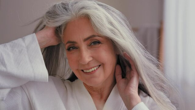 Female portrait close up headshot 60s old middle-aged mature senior aging Caucasian woman grandma senior older 50s lady model with long shiny smooth gray hair smiling looking at camera wind haircare