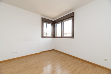 Empty living room with wooden laminate flooring with bare white walls and two brown anodized aluminum corner windows