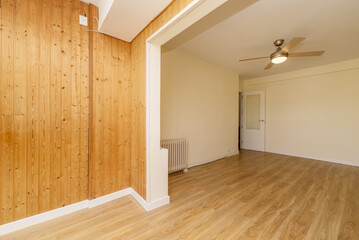 Empty living room with oak laminate flooring with honey pine tongue and groove walls and ceiling fan