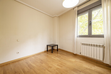 Empty living room with French oak parquet floors with plain white painted walls and a window with a radiator and white curtains
