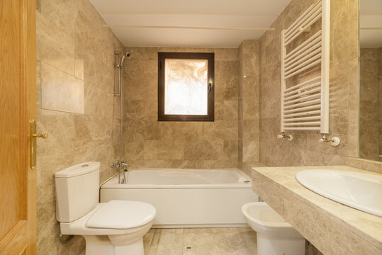 Bathroom with mirrors clad in marble, cream marble floors with matching countertop with porcelain base and white resin bathtub with heated towel rail