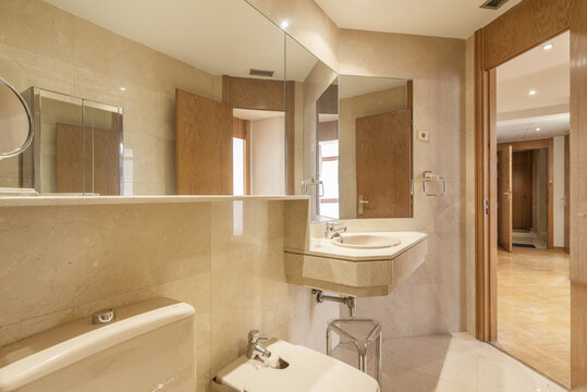 Bathroom with large mirrors on the walls that are clad in cream marble and floors of the same