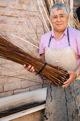 Latin old man holding a bunch of wet willow sticks for making wicker craft art. Tradition and culture of South America