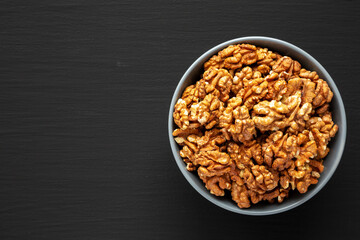 Raw Organic Walnuts in a Bowl on a black background, top view. Flat lay, overhead, from above. Copy space.