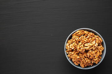 Raw Organic Walnuts in a Bowl on a black background, top view. Flat lay, overhead, from above. Space for text.