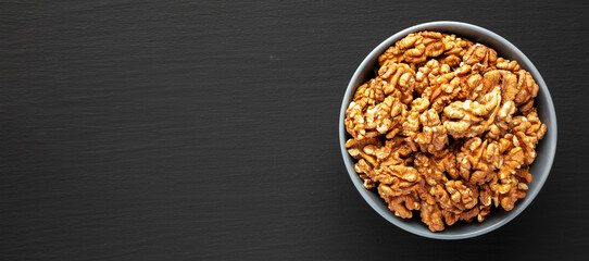 Raw Organic Walnuts in a Bowl on a black background, top view. Flat lay, overhead, from above. Copy space.