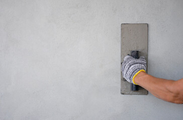 worker hand holding trowel is plastering cement wall