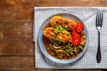 Green beans with champignons and cutlets sprinkled with green onions in a plate on a wooden table on a gray checkered napkin next to a fork.