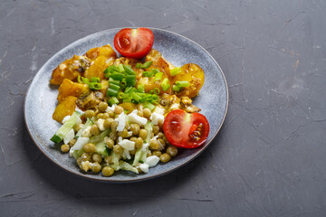 Baked potatoes with cheese and mushrooms garnished with cherry tomatoes sprinkled with green onions in a plate on a gray background.copy space