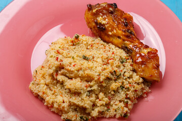 Couscous with vegetables in sauce and spices with grilled chicken drumstick on a plate close-up.
