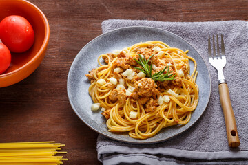 Homemade bolognese pasta on a plate next to a fork and a napkin on the table are tomatoes and dry pasta.