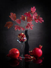 Modern still life with pomegranates and autumn leaves on a dark background