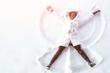 African smiling woman lies on snow drawing snow angel figure in winter day, sunlight