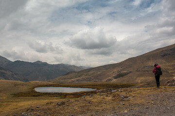 Fototapeta premium Woman with motorbike helmet next to a small rain pond, in Abra de Lares, view of the mountains and the valley, in Peru. 