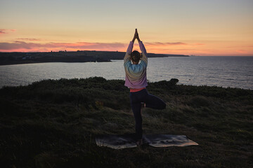 Fototapeta na wymiar attractive woman practicing yoga at sunrise in front of the ocean.