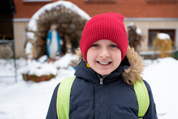 portrait of a happy boy stands in front of the statue of the holy virgin mary near the temple in winter