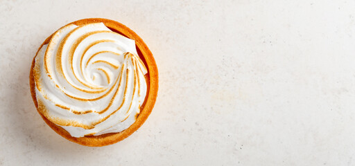 Overhead shot of a small lemon meringue tartover light background with space for text © mariashumova