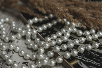A string of pearls, a magazine and dried flowers lie on a newspaper, a photo in an elegant retro style.
