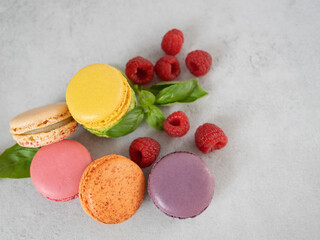 multi-colored macaroons and raspberries on a gray background . French dessert and red berries.