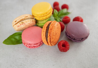 multi-colored macaroons close-up and raspberries on a gray background . French dessert and red berries.