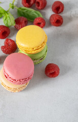 raspberries and colored macrons on a gray background with copy space. Vertical photo of raspberries and cookies