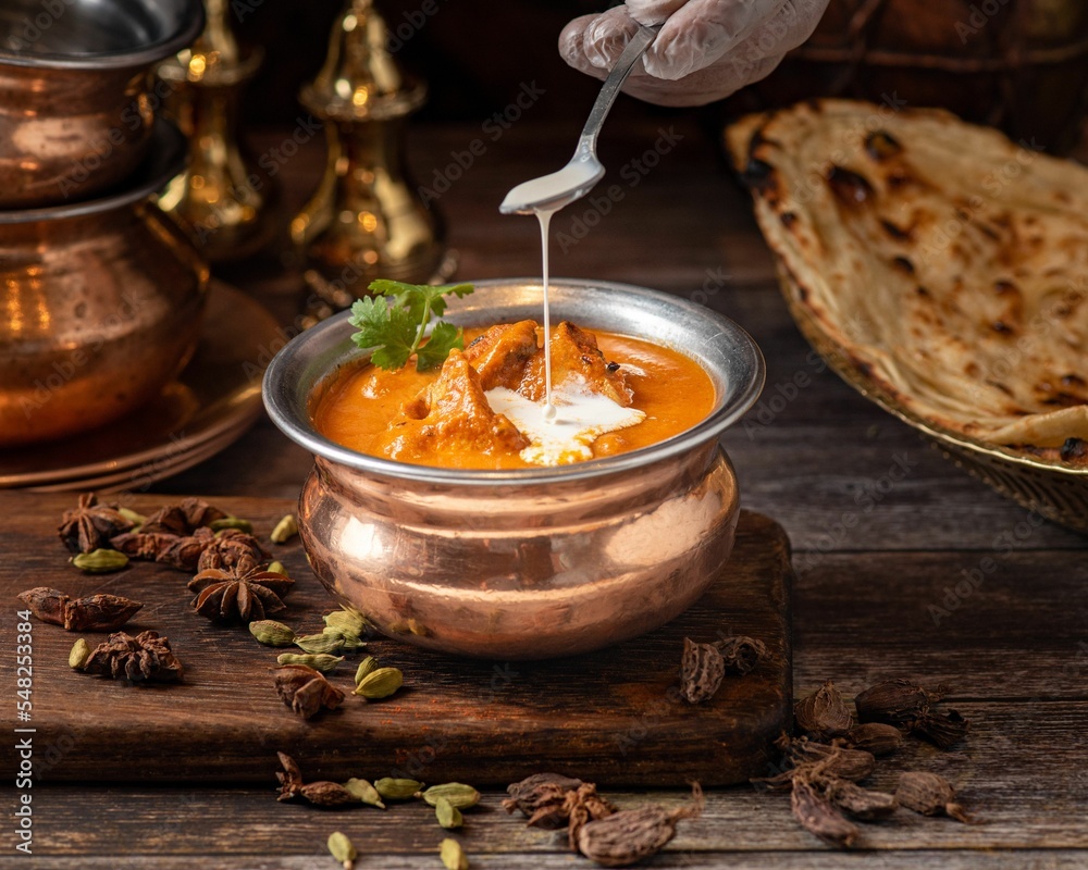 Poster closeup shot of an indian buttered chicken dish in a bowl on a wooden board