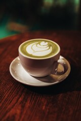 A cup with green Japanese matcha tea and milk foam on a wooden table