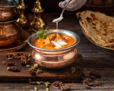 Closeup shot of an Indian buttered chicken dish in a bowl on a wooden board