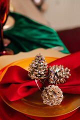 fir cones, decorated with sparkles and plastic rhinestones, lie on a red napkin on a yellow plate, background in blur