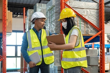 Two smile warehouse workers in uniforms and yellow helmets on heads standing and talking about job. adviser