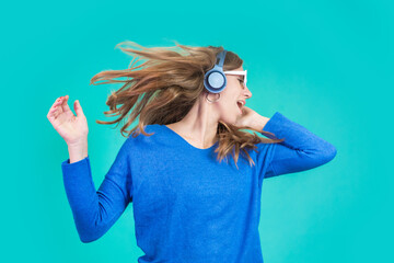 Gorgeous girl singing and listening music in headphones on blue background. Woman dancing with hair waving and eyes closed