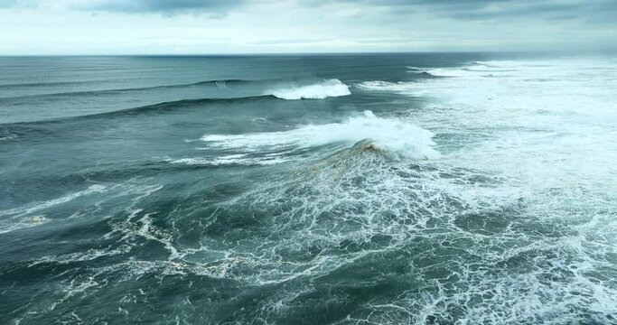 Aerial view of powerful dark ocean waves rolling from above. Drone flying over fabulous sea tide on a stormy day. Breaking surf with foam in Atlantic ocean. Big swell in Nazare, Portugal.