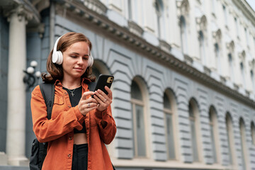 Woman in headphones using her mobile phones while walking around the city, checking email, online chatting, mobile travel map.