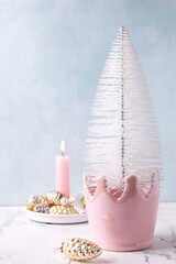 Winter holidays postcard. White decorative tree , pink burning candle, golden and silver decorative cones against blue  textured wall.  Pink and golden Christmas. Selective focus. Place for text.