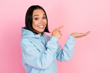 Photo of cute pretty girl dressed blue sweatshirt pointing holding arm empty space isolated pink...