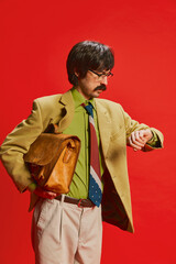 Portrait of stylish man with moustache posing in vintage suit isolated over red background. Being late for work